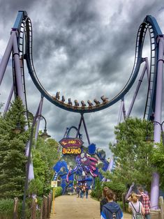 people are walking down the walkway at an amusement park with roller coasters on it