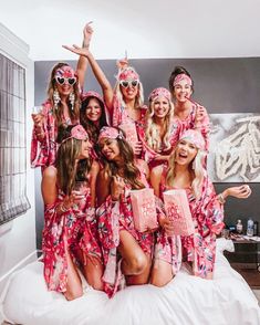 a group of women in matching pink robes posing on a bed with their arms up