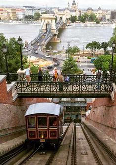 a train traveling down tracks next to a bridge and river with people standing on it