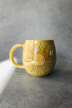 a yellow coffee cup with the sun painted on it's side, sitting on a gray surface