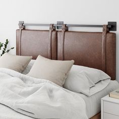 an unmade bed with white linens and wooden headboard, in a bedroom