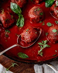 meatballs covered in marinara sauce and garnished with fresh herbs on a spoon