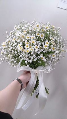 a person holding a bouquet of daisies in their hand with ribbon around the wrist