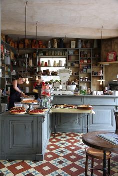 a woman preparing food in a kitchen next to a table with two pizzas on it