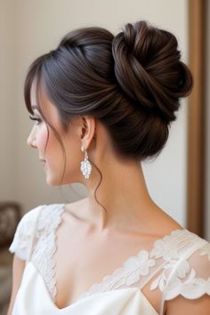 a woman with her hair in a low bun, wearing a white dress and earrings