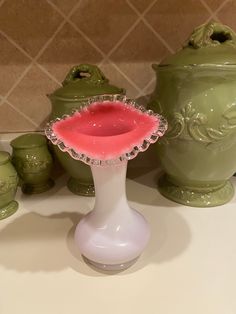 there is a vase with a pink substance in it next to other green items on the counter