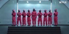 five men in pink suits stand on steps with their backs turned to the camera, wearing helmets and goggles