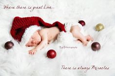 a newborn baby wearing a santa hat and laying on a white fur rug with ornaments around it