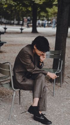 a man sitting on a chair in the park talking on his cell phone while holding his hand to his face