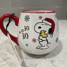 a red and white coffee cup with a snoopy christmas mug on it's side