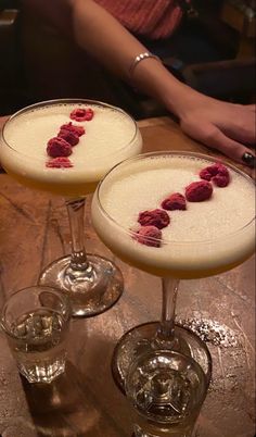 two martinis with raspberries sit on a table in front of a woman