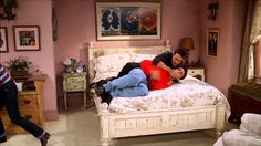 a man and woman laying on top of a white bed in a room with pink walls