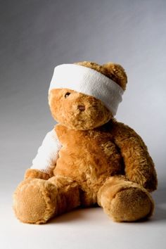 a brown teddy bear with a bandage on its head sitting in front of a gray background