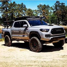 a silver truck parked in the dirt near some trees