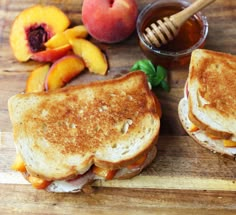 two grilled sandwiches sitting on top of a wooden cutting board next to peaches