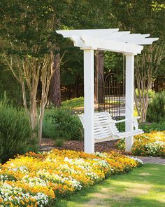 a white bench sitting in the middle of a flower garden with yellow and white flowers