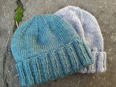 two knitted hats laying on the ground next to each other, one blue and one white