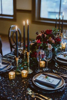 the table is set with black and gold plates, silverware, candles, and flowers