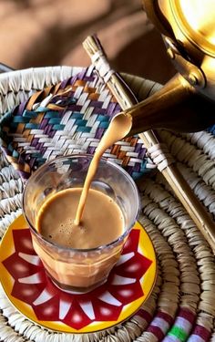 a cup of coffee is being poured into a saucer on a colorful plate with gold spoons