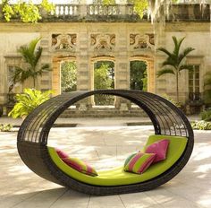 an outdoor lounge chair with pink and green pillows in front of a stone courtyard area