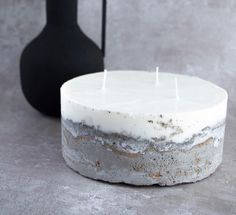 a white cake sitting on top of a table next to a black vase and candle