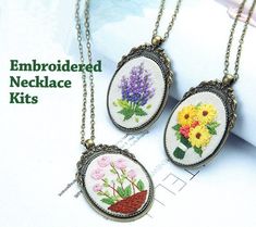 two embroidered necklace kits with flowers in them on a white tablecloth and gold chain