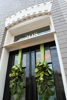 two green wreaths on the front door of a brick building with black double doors