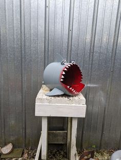 a toy shark with its mouth open sitting on top of a small white table in front of a metal wall