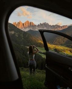 a woman standing in the window of a car looking out at mountains and valleys with trees