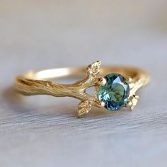 a gold ring with a blue stone in the center and leaves on it's side