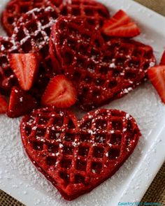 heart shaped waffles with strawberries and powdered sugar on the top are ready to be eaten