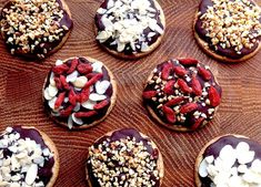 chocolate covered donuts with nuts and other toppings on a wooden surface, ready to be eaten