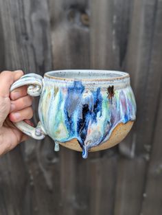 a hand holding a ceramic mug with blue and green designs on it's side