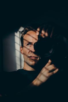 a man holding a camera up to his face with the sun shining through the window behind him