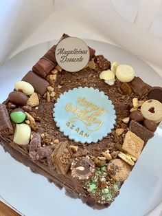 a square cake with chocolate, cookies and candies on it sitting on a white plate