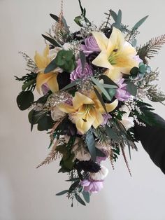 a bridal bouquet with yellow lilies and greenery is held by someone's hand