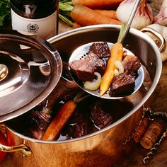 a pot filled with meat and carrots next to some bottles of wine on a table