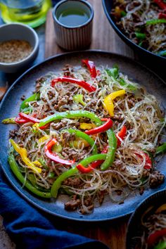 a plate with noodles, peppers and meat on it next to bowls of dipping sauces