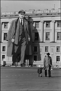 a man and child are walking in front of a building with a giant poster on it