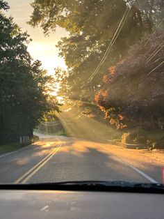 the sun shines brightly through the trees on an empty road as seen from inside a car