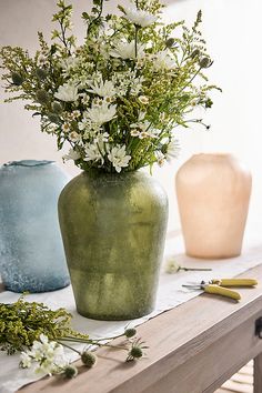 two vases with flowers in them sitting on a table next to scissors and other items