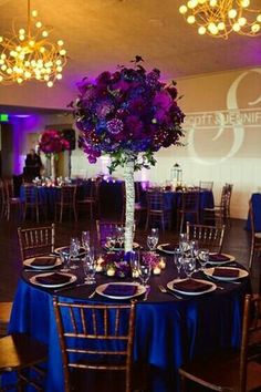 an elegant centerpiece with purple flowers in a tall vase on top of a round table