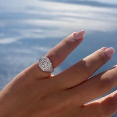 a woman's hand with a diamond ring on top of her finger and water in the background