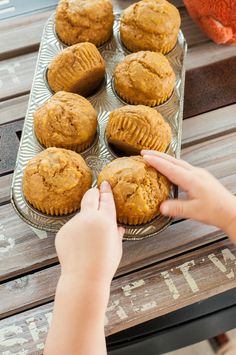 a person reaching for some muffins on a tray