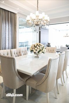 a white dining room table surrounded by beige upholstered chairs and a chandelier