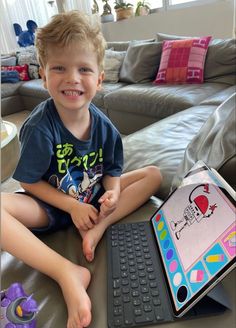 a young boy sitting on the floor next to a keyboard and laptop computer, smiling at the camera