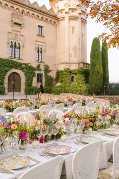 an outdoor table set up with plates and flowers for a formal dinner in front of a castle