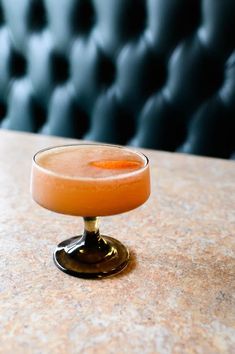 an orange drink sitting on top of a table next to a black leather chair in the background