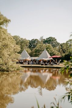 several tents are set up on the edge of a body of water with trees in the background