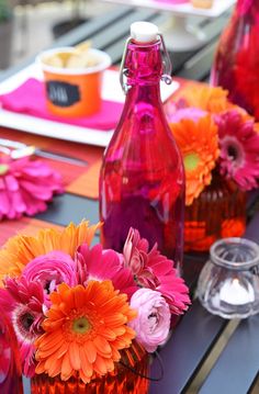 colorful flowers in vases sitting on a table with plates and utensils next to them